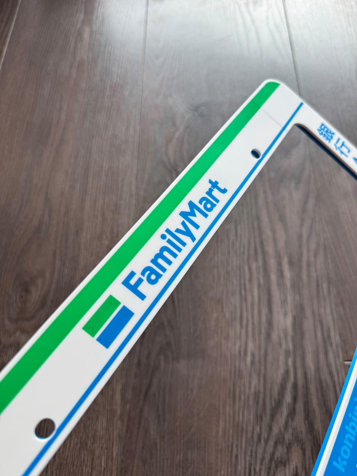 Close-up of the top rail of the Family Mart license plate frame with the FamilyMart logo and green stripe